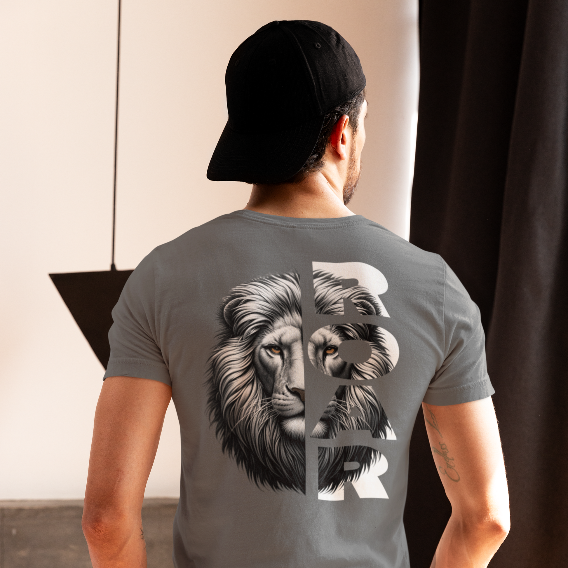 Person wearing a gray t-shirt with a lion graphic on the back, standing indoors.